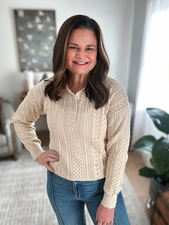 Woman wearing a beige knitted sweater and blue jeans indoors.