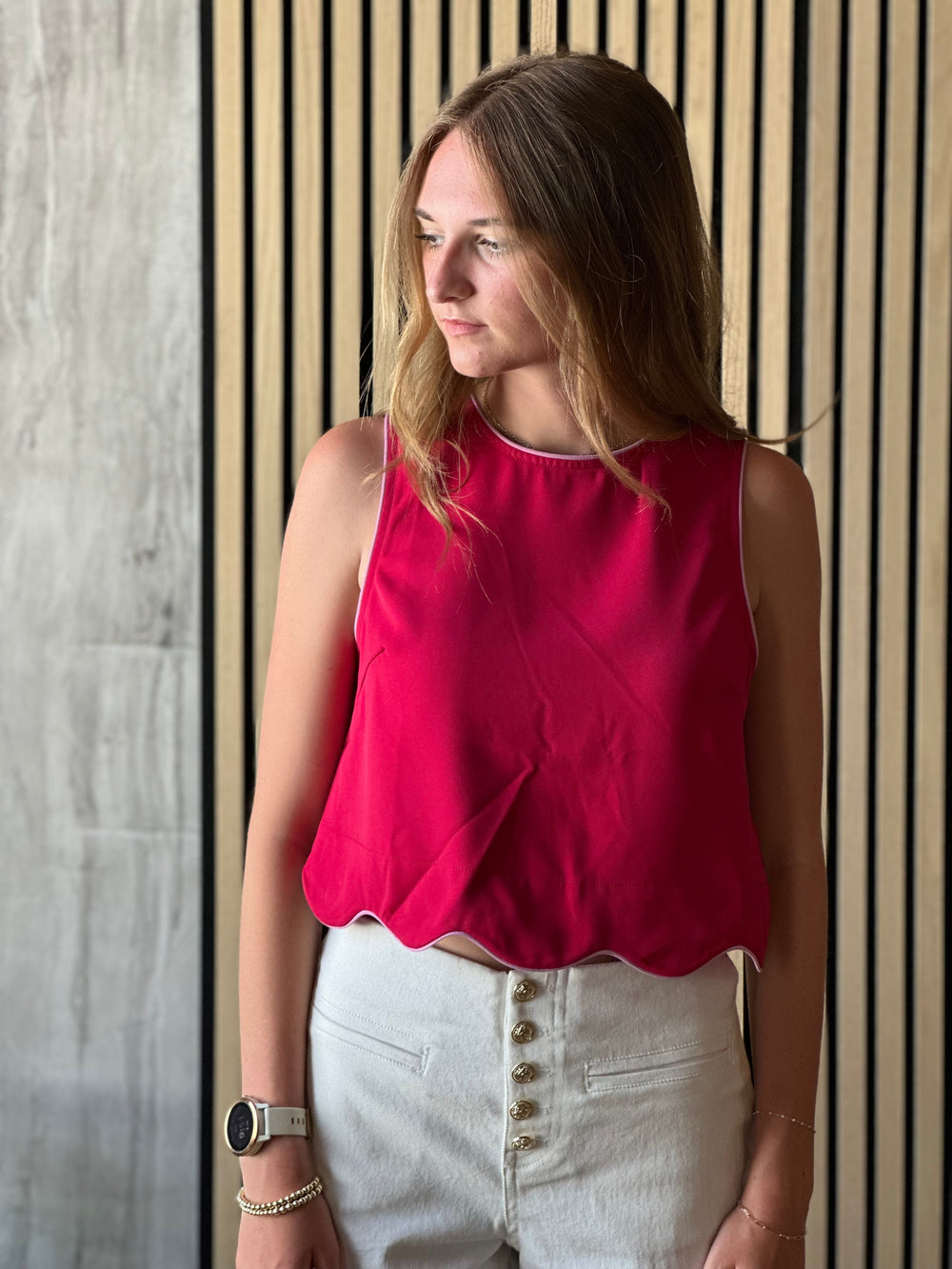 Front view of model wearing a scarlet colored top with a sleeveless design and scalloped hem and a button closure on the back of top