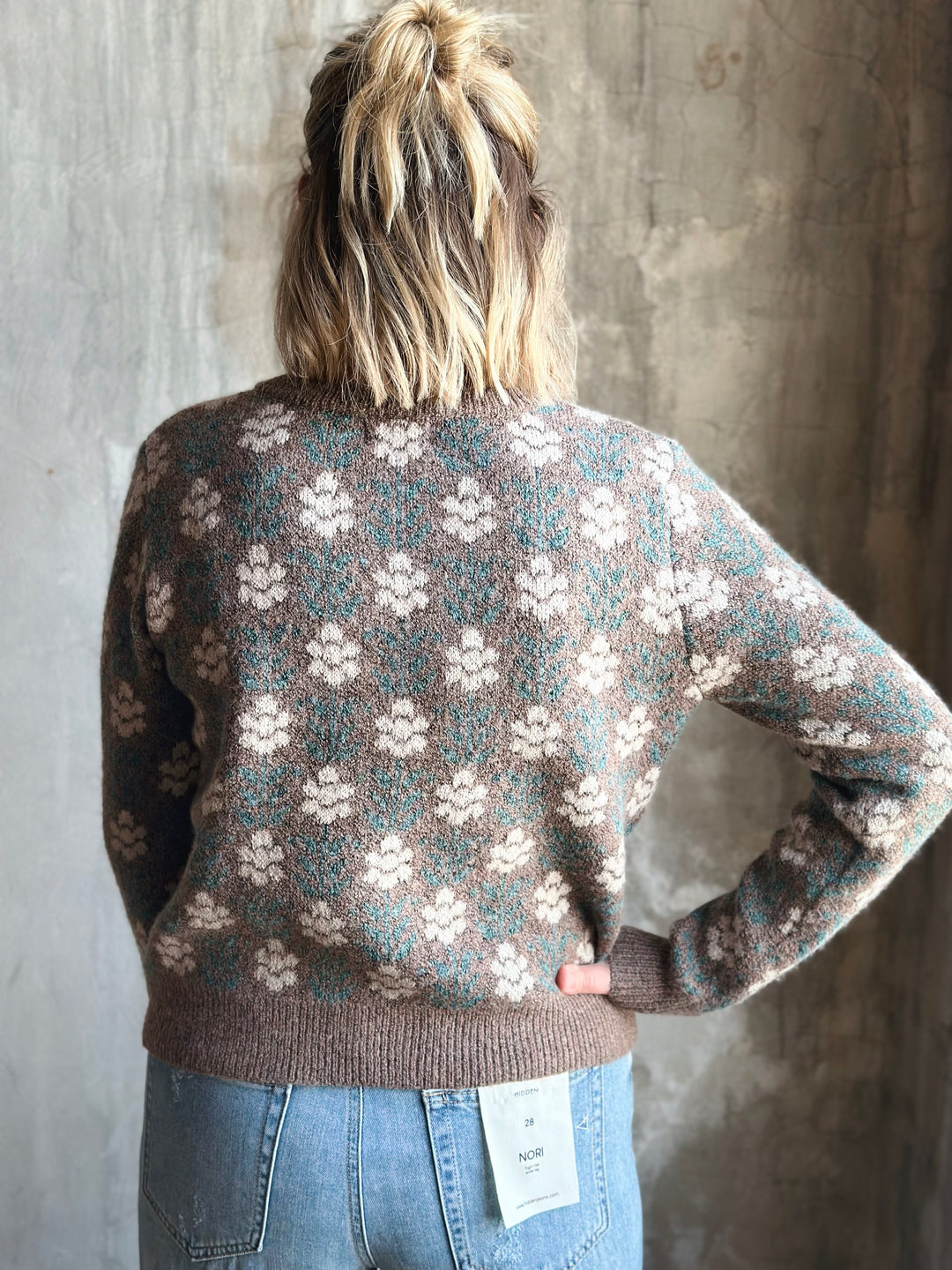 Person wearing a patterned sweater with a concrete wall background