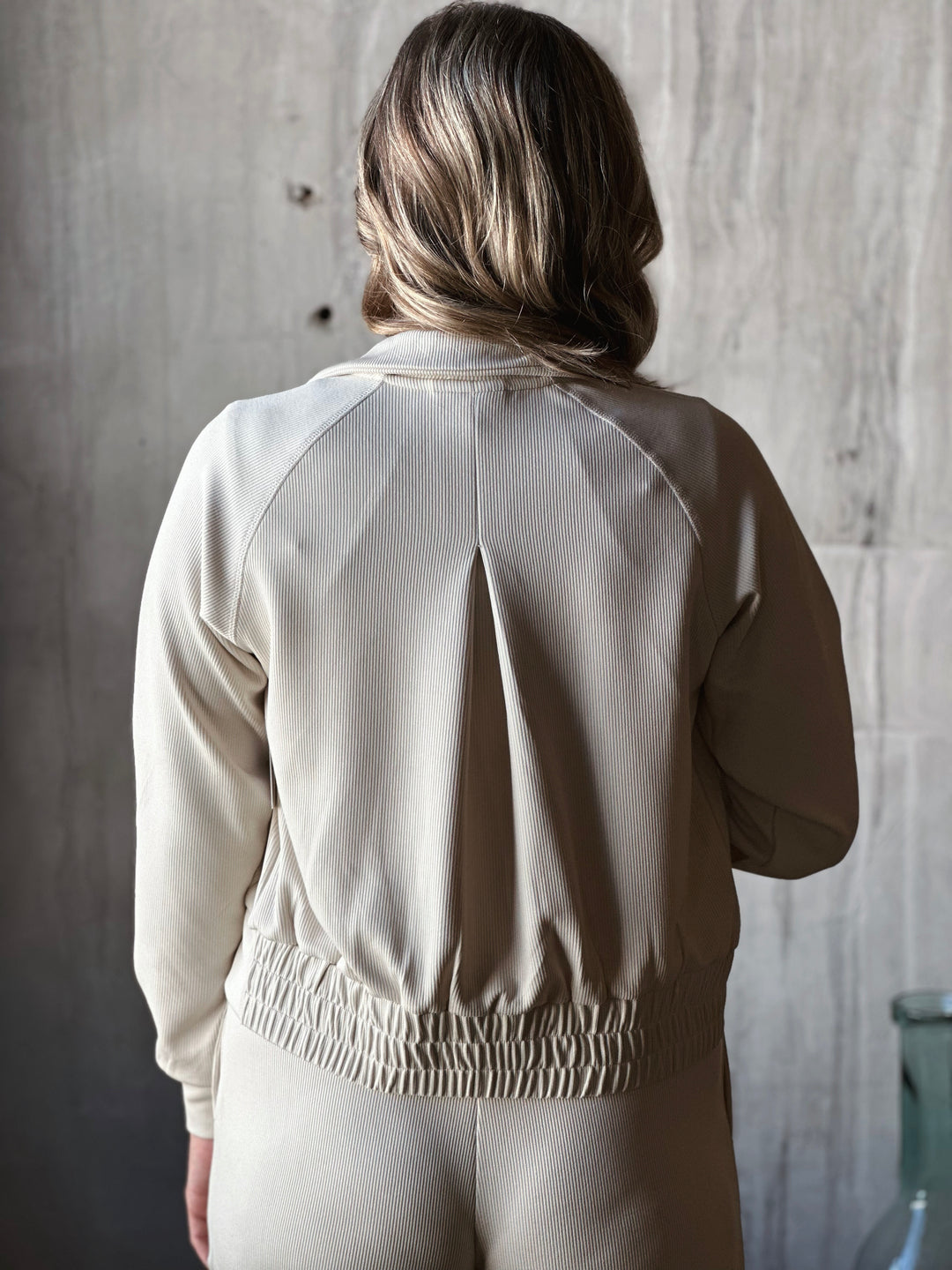 Person wearing a beige tracksuit against a textured wall.