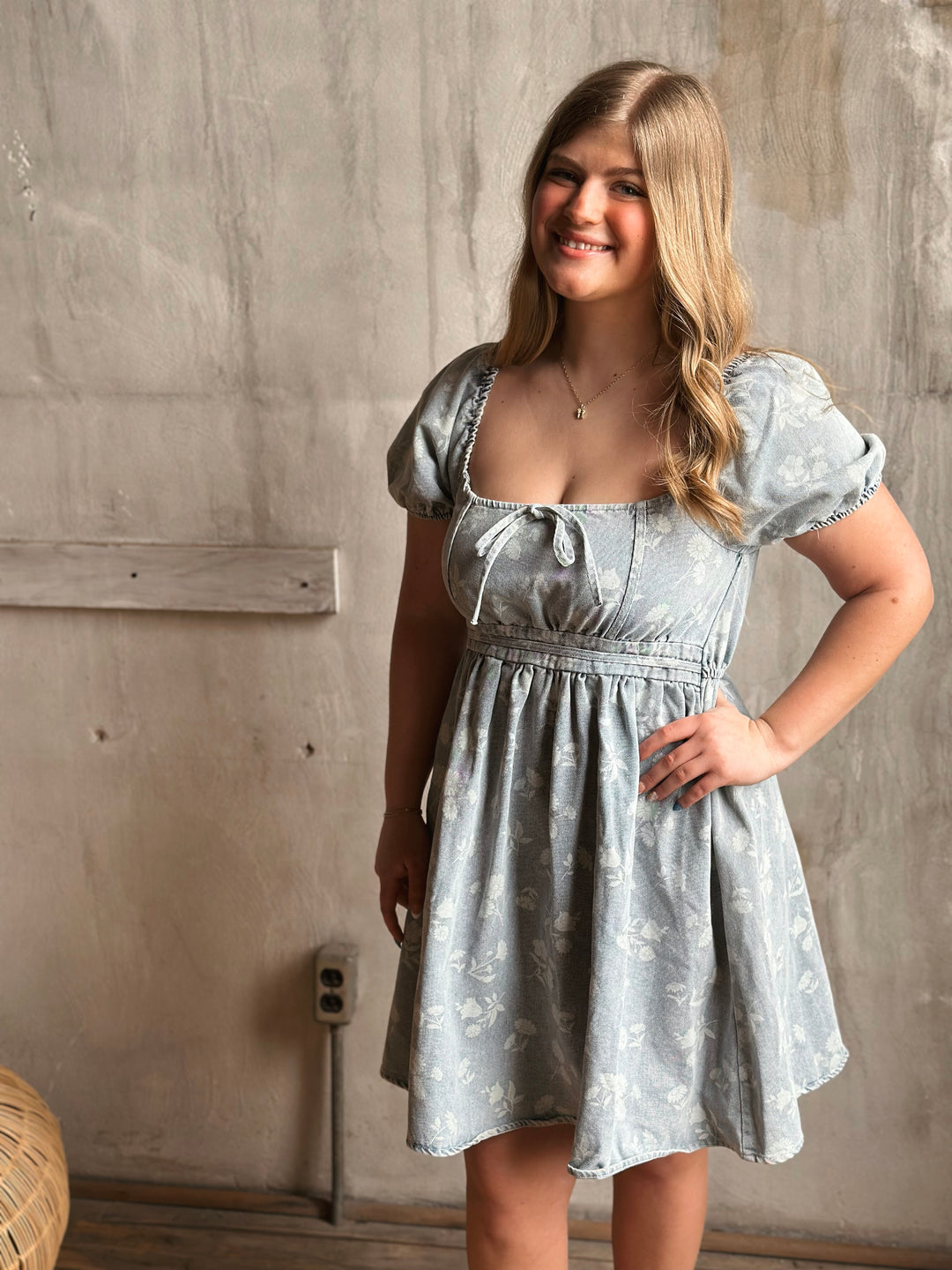 Woman wearing a light blue dress with puffed sleeves against a textured wall.