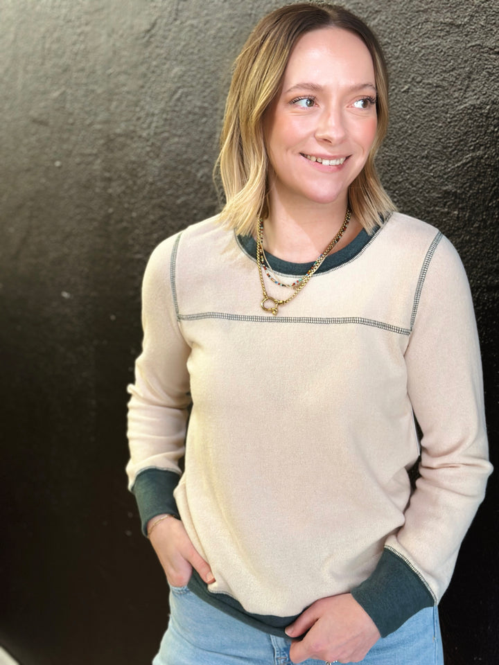Woman wearing a beige sweater with green accents against a dark background