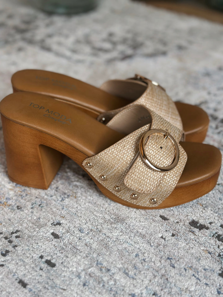 Pair of gold sandals with wooden block heels on a textured surface.