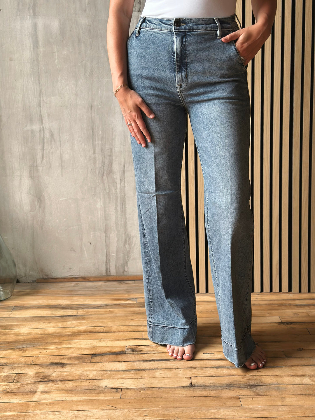 Person wearing blue jeans standing on a wooden floor with a neutral wall background