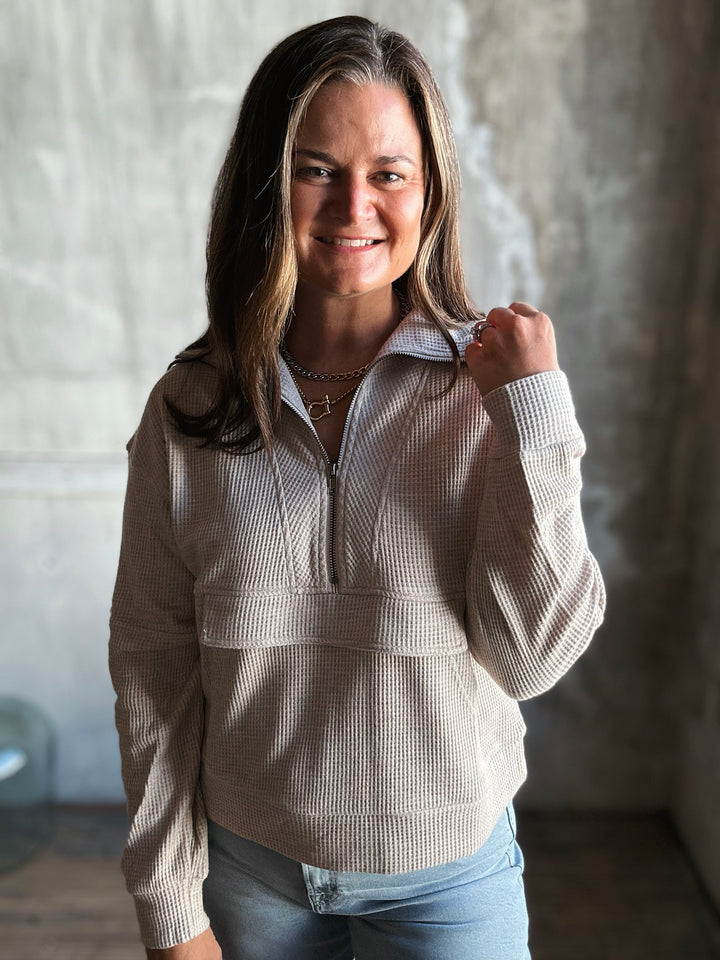 Woman wearing a beige sweater with a zipper, standing against a neutral background