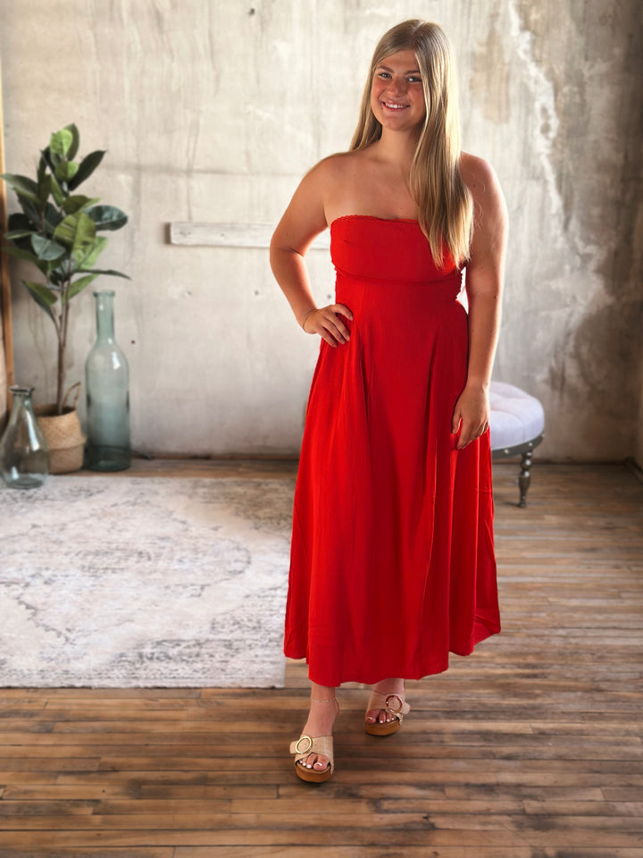 Woman in a red strapless dress standing in a room with wooden floor and white walls.