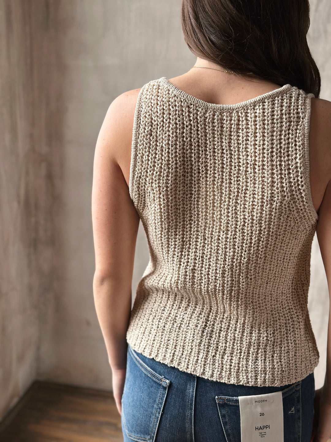 Person wearing a beige knitted tank top with a plain background