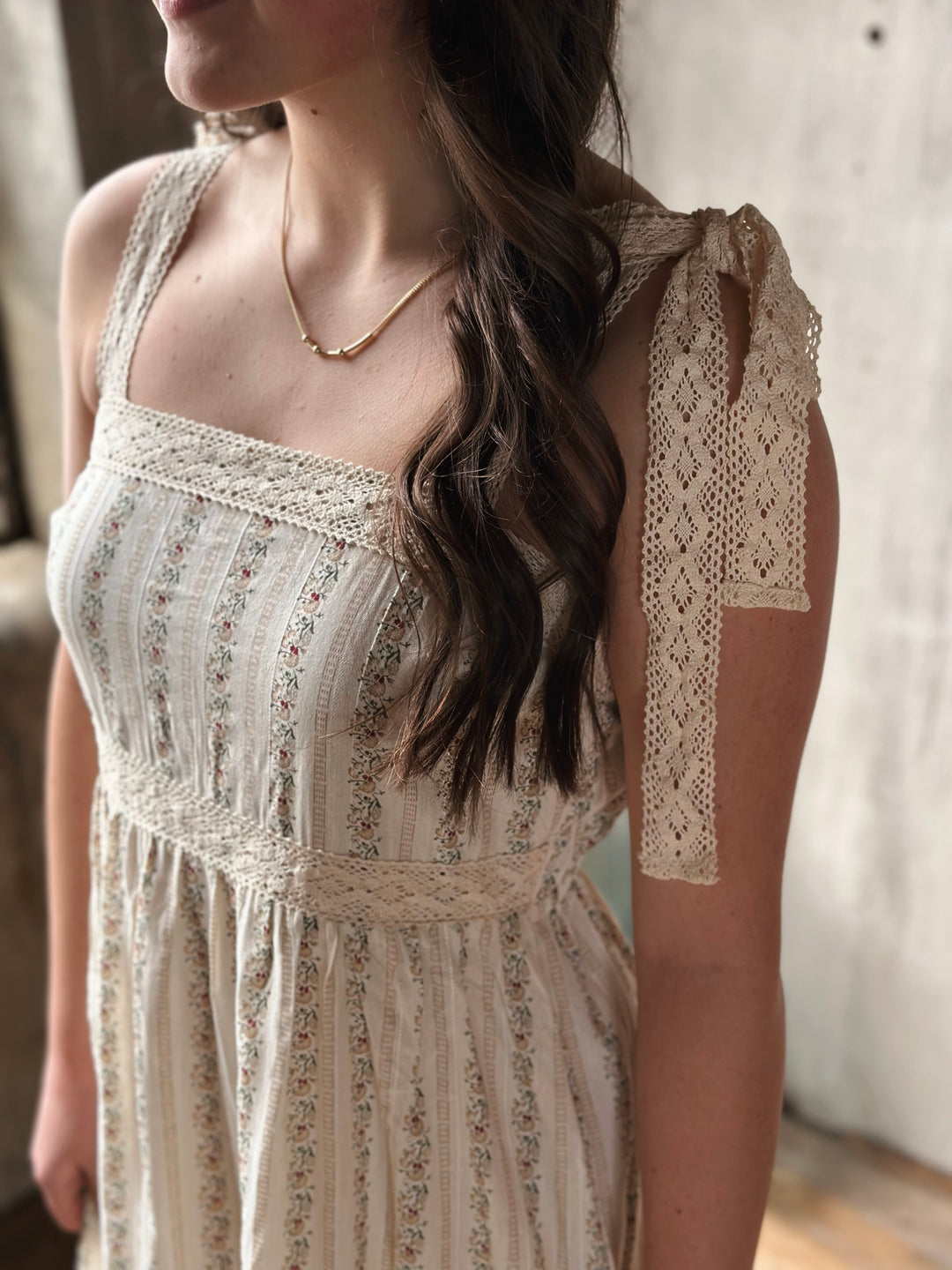 Woman wearing a lace-trimmed dress with floral designs with a neutral background.