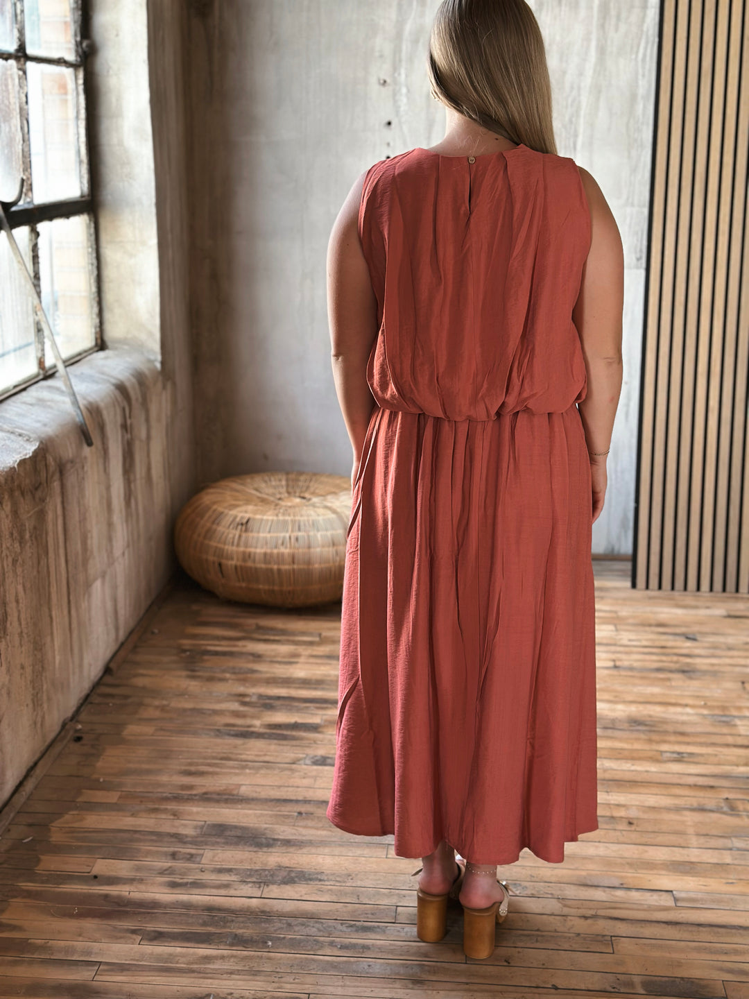 Woman wearing a rust-colored skirt and sleeveless top set standing in a room with wooden floor and window.