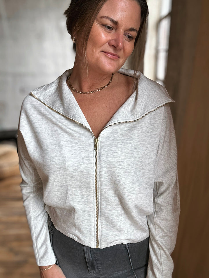 Woman wearing a light gray zip-up hoodie with a neutral background