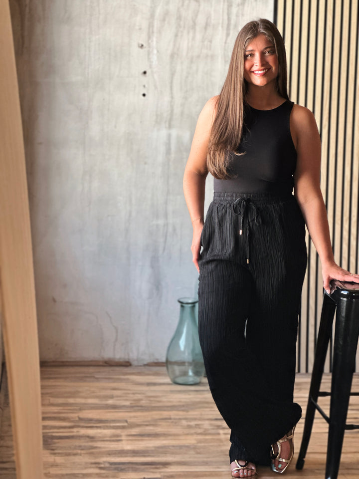 Woman in a black outfit standing indoors with a neutral background