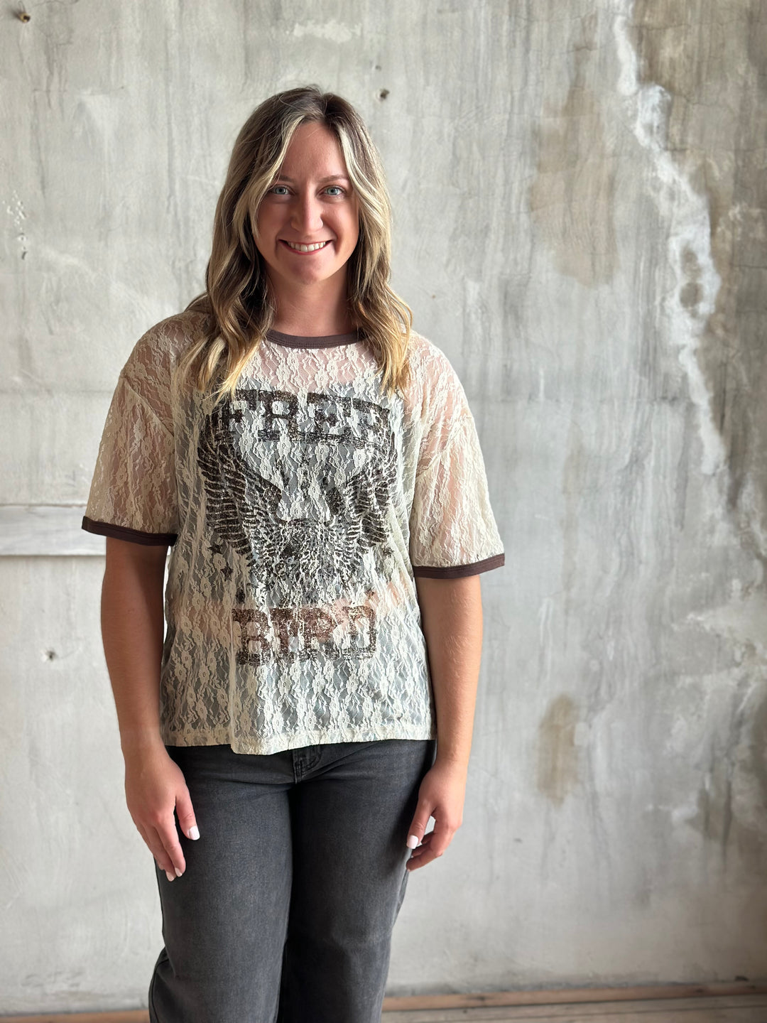 Woman wearing a cream lace graphic tee with gray jeans, front view
