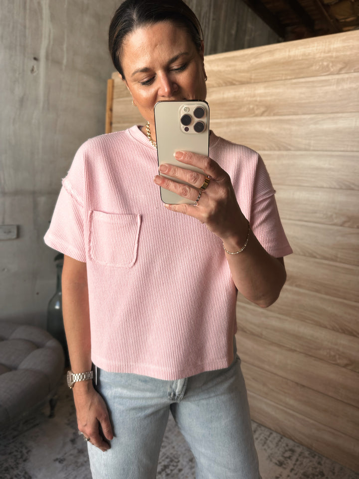 A woman wearing a textured light pink short sleeved shirt with a pocket on the left side of the shirt. 