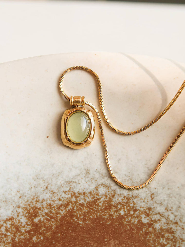 Gold necklace with a green pendant on a textured surface