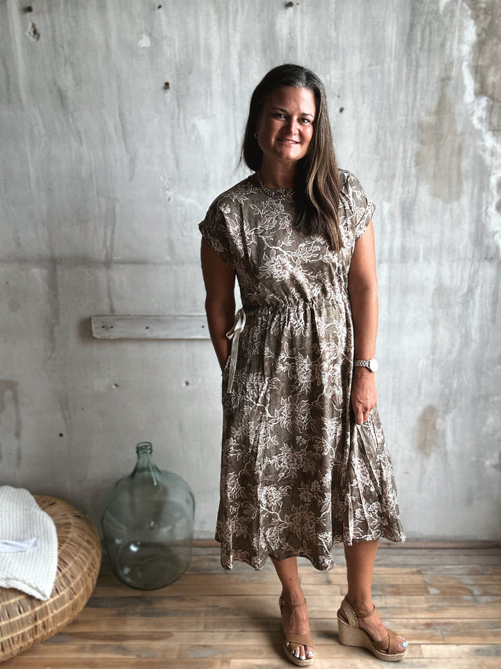 Woman wearing a patterned dress standing against a textured wall.
