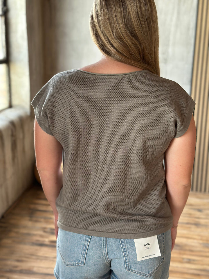 A person wearing a brown textured top and light blue denim shorts.