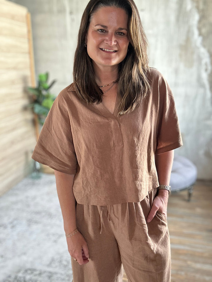 Woman wearing a brown outfit standing indoors with a blurred background.