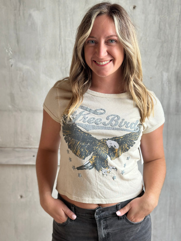 Woman wearing a cream Free Bird eagle graphic tee with jeans