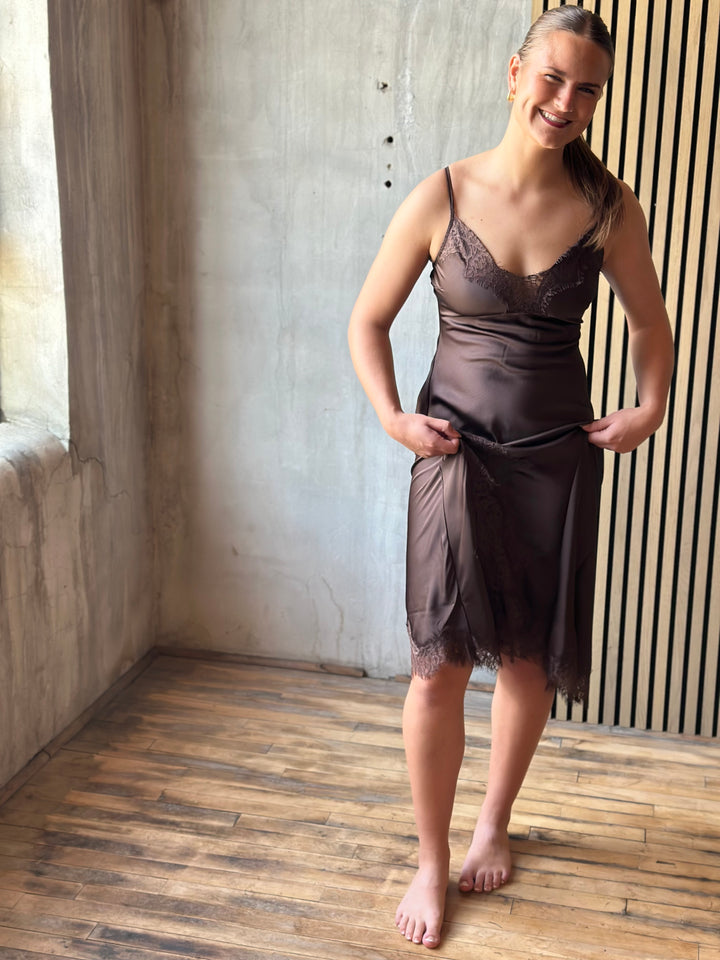 Woman wearing a chocolate brown satin slip dress with lace trim, front view