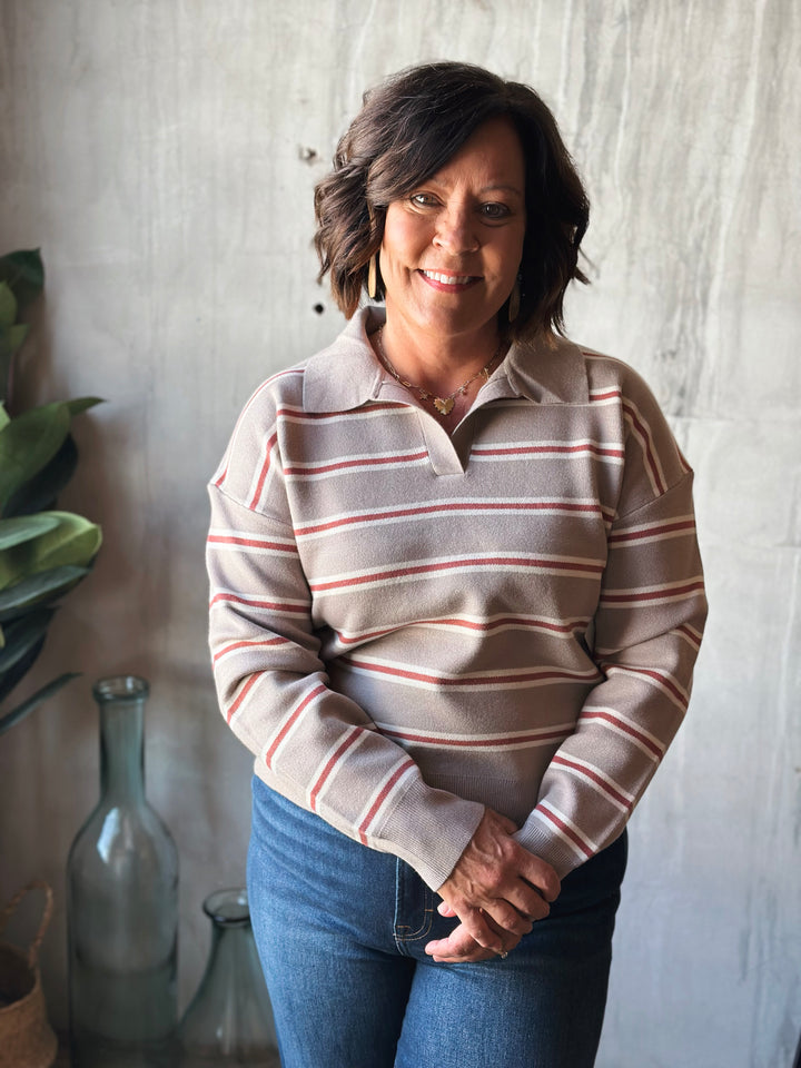 Woman wearing a striped sweater and jeans standing against a neutral wall.
