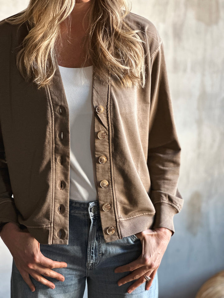 Person wearing a brown button-up jacket over a white shirt and jeans against a neutral background