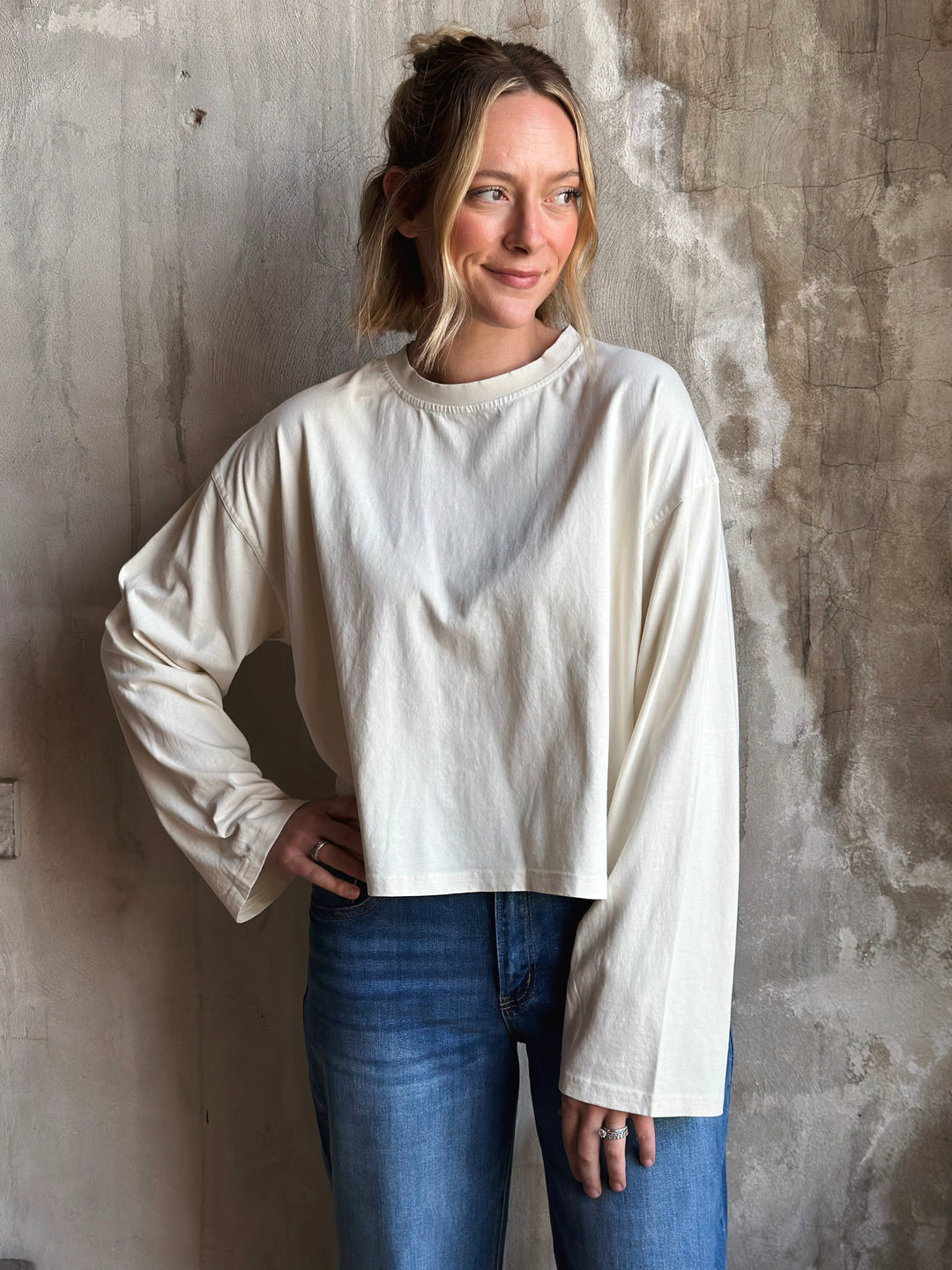Woman wearing a white oversized sweater and blue jeans against a textured wall.