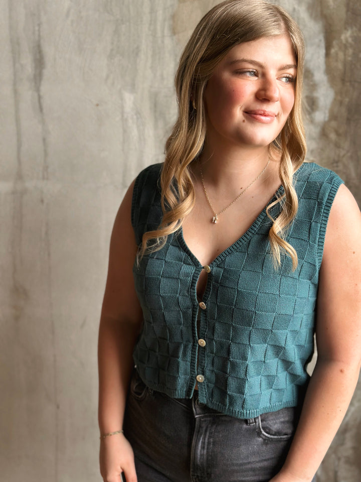 Woman wearing a teal checkered vest against a neutral background