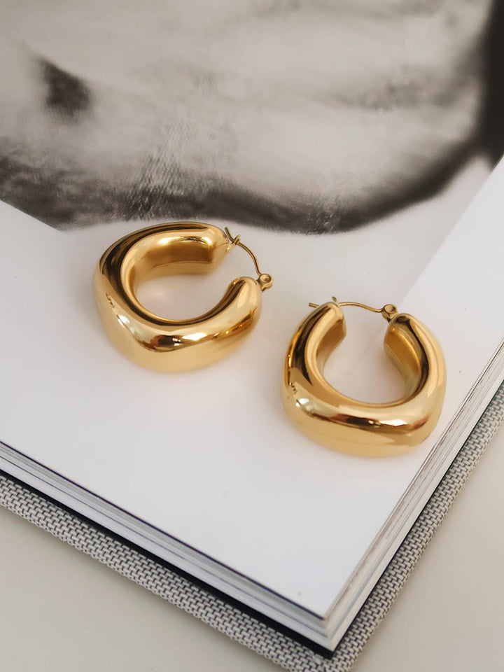 Gold hoop earrings on a white surface with a blurred background