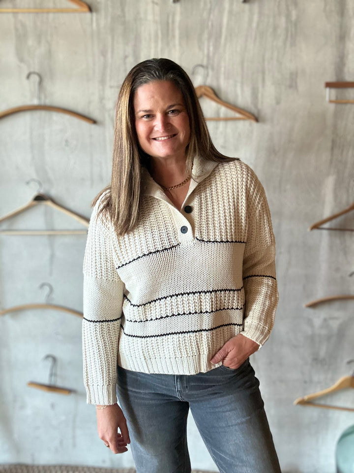 Woman in a cream collared sweater and jeans, angled view