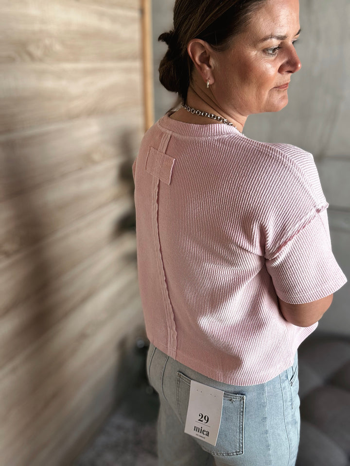 A woman wearing a textured light pink short sleeved shirt.