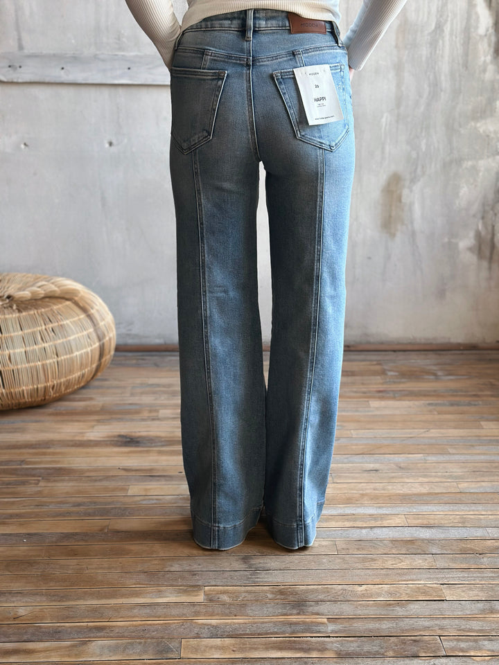 A person wearing blue flared jeans standing on a wooden floor.