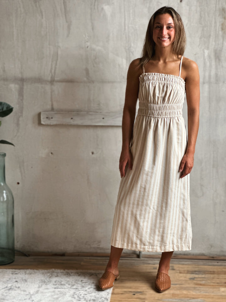 Woman wearing a white and cream striped dress standing against a concrete wall.