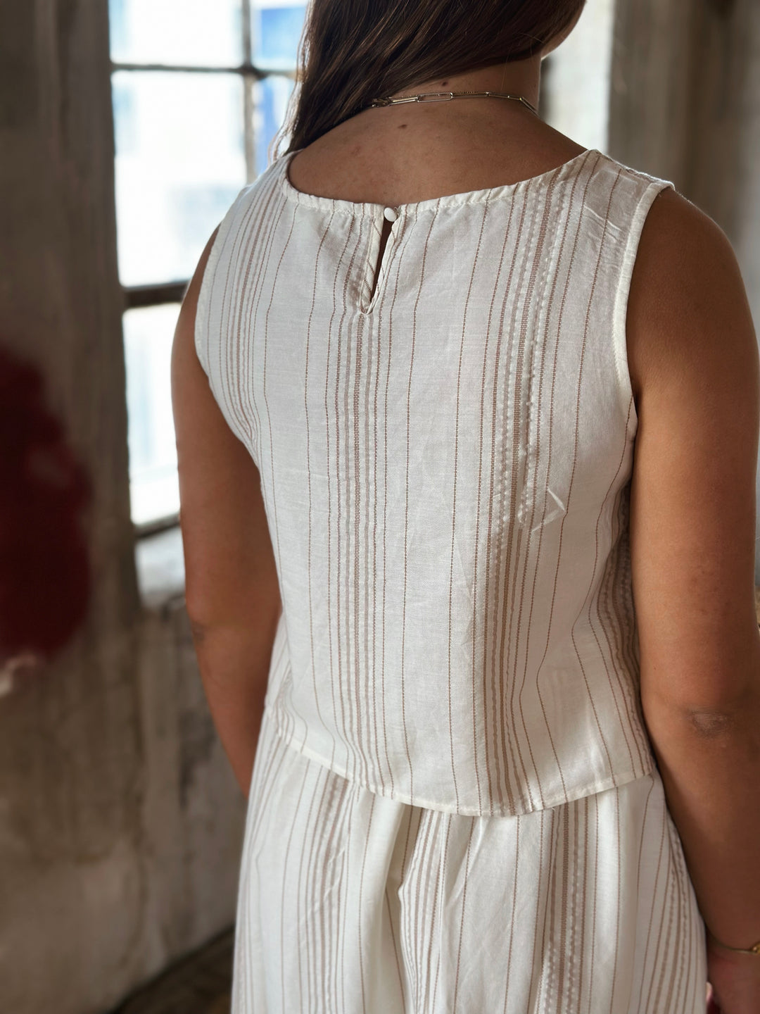 A person wearing a white and beige striped top in a softly lit room.