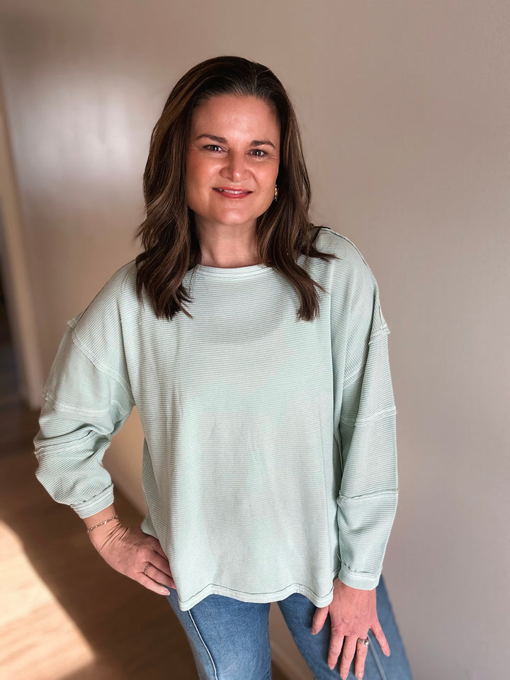 Woman wearing a light green sweater and blue jeans indoors.