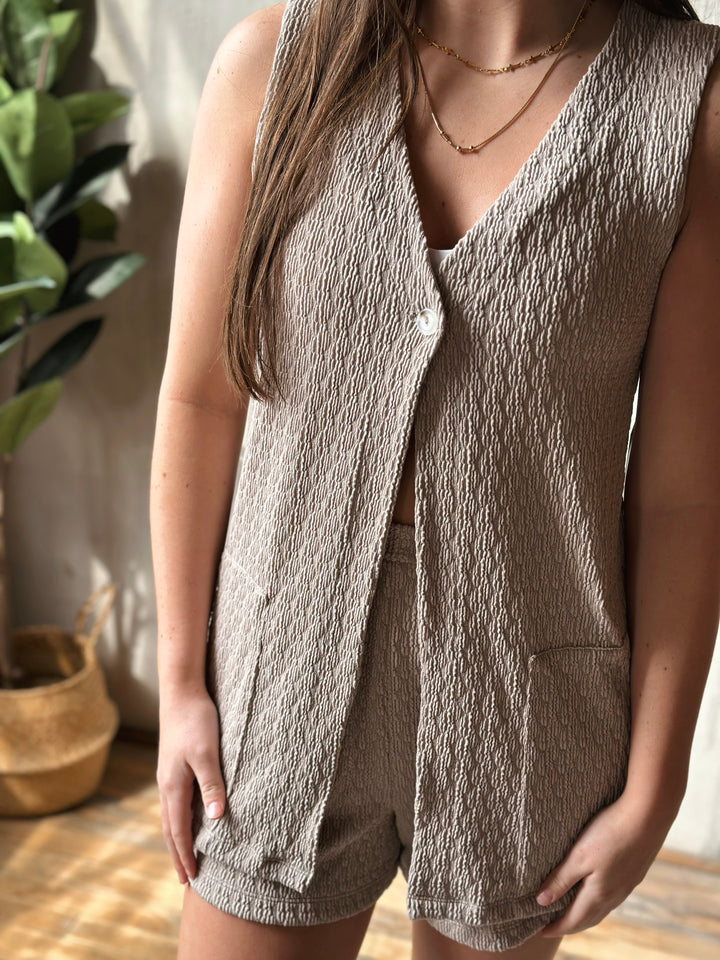Person wearing a textured beige vest and shorts set with a plant in the background