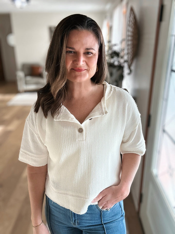 Woman wearing a white blouse with short sleeves and blue jeans indoors.