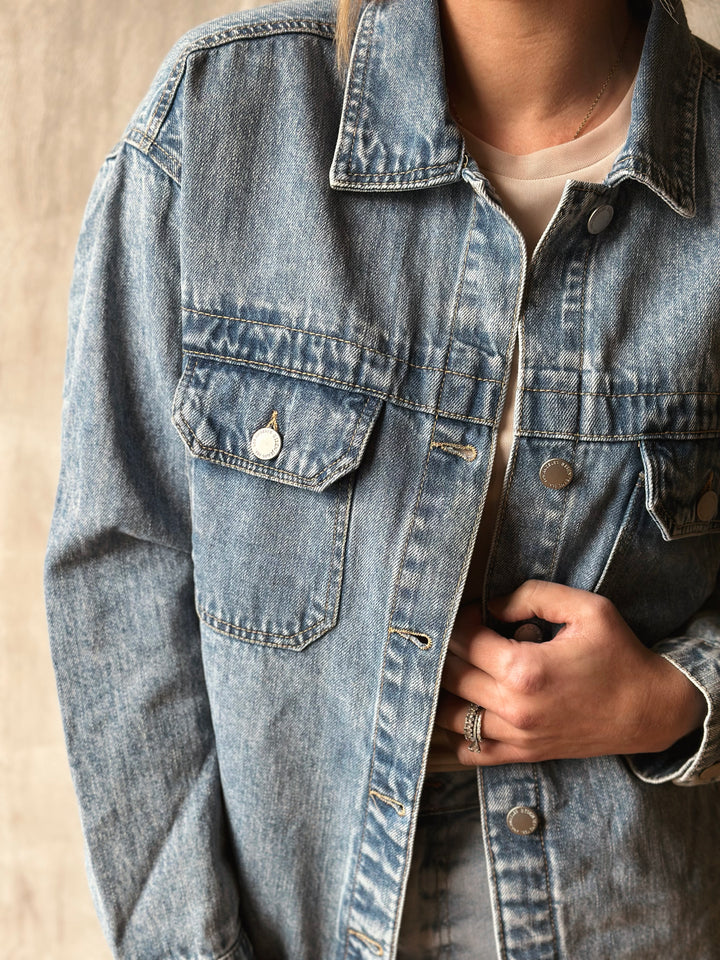 Close-up of a person wearing a light blue denim jacket on a neutral background