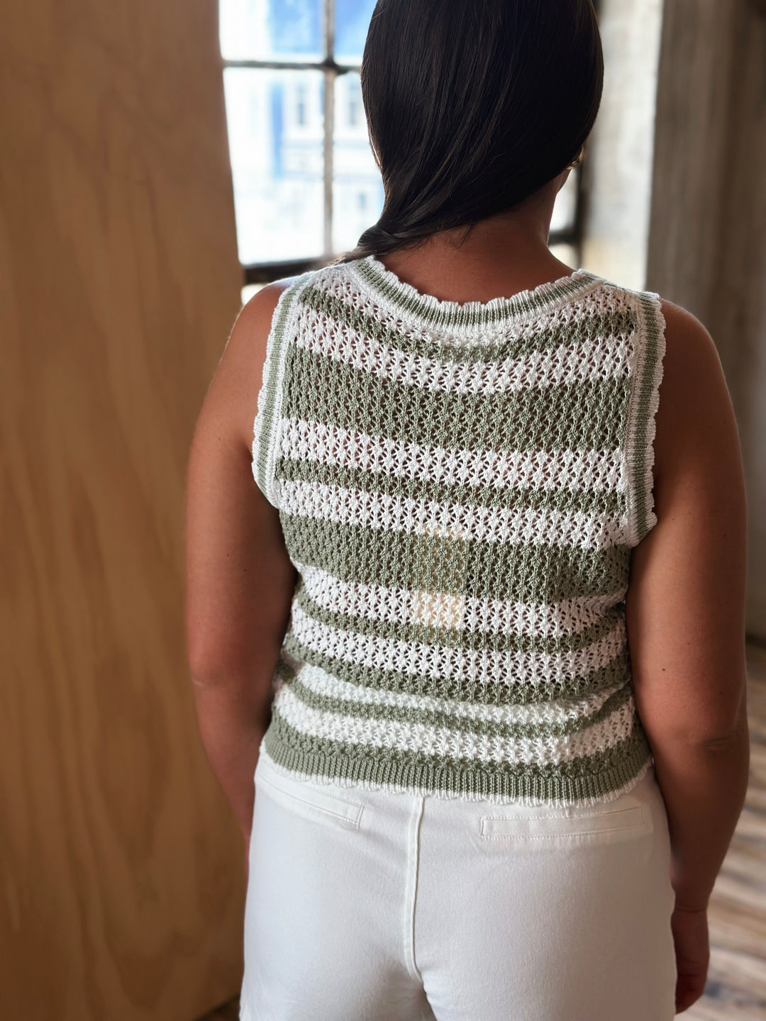 Person wearing a green and white striped sleeveless sweater in a room with wooden walls.