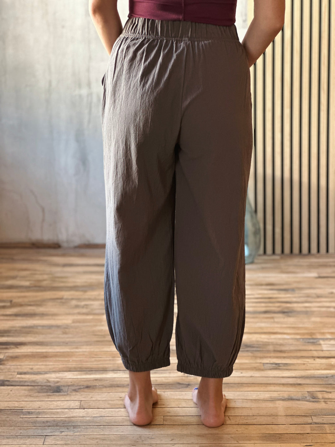 Person wearing brown wide-leg pants on a wooden floor with a neutral background