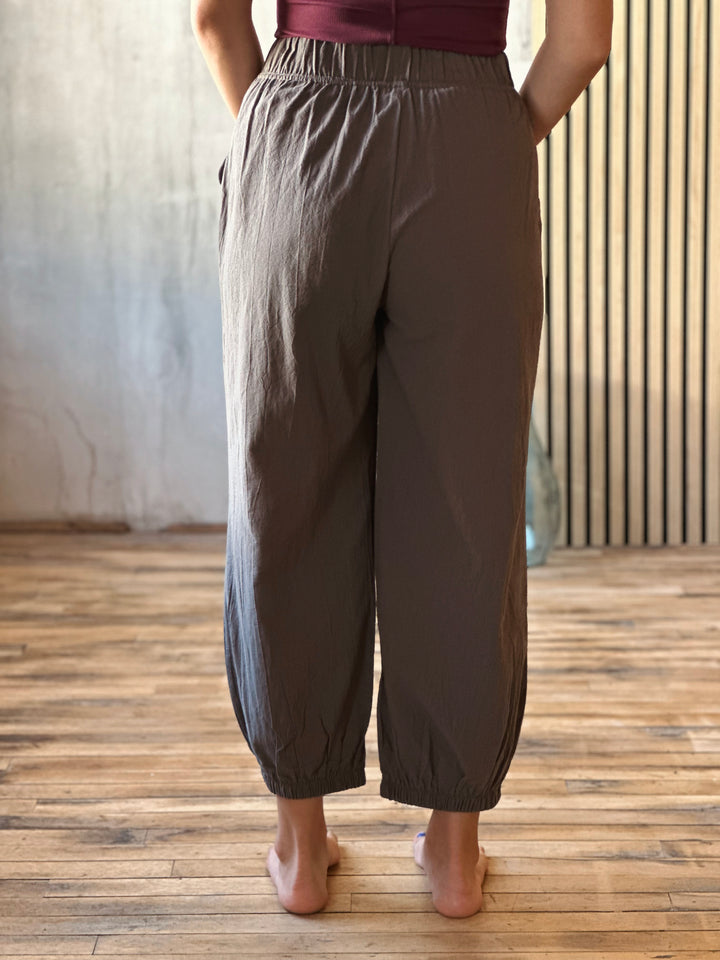 Person wearing brown wide-leg pants on a wooden floor with a neutral background