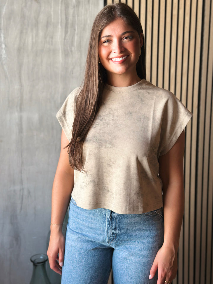 Woman wearing a beige top and blue jeans standing against a textured wall.