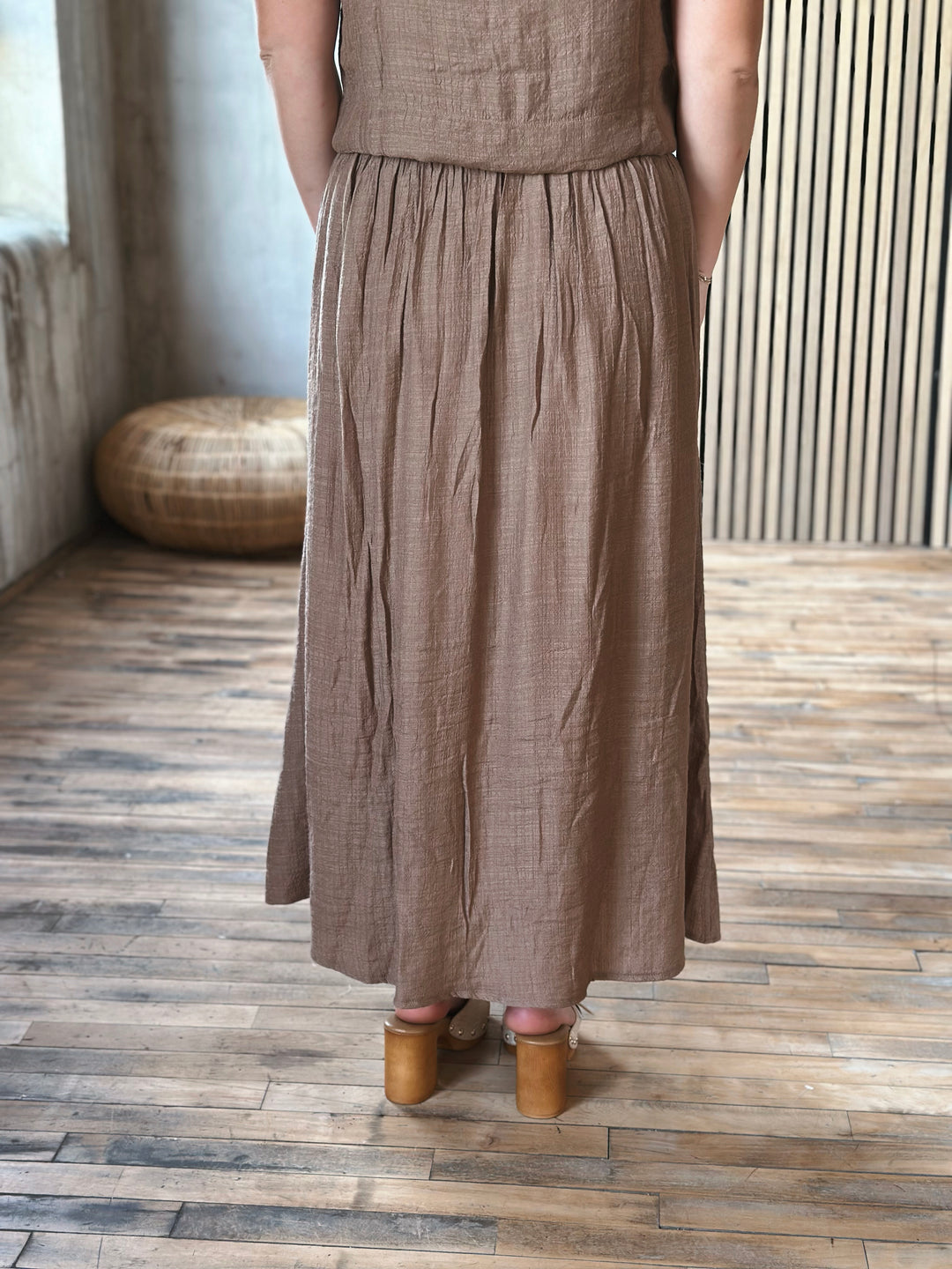 A person wearing a brown skirt standing on a wooden floor.