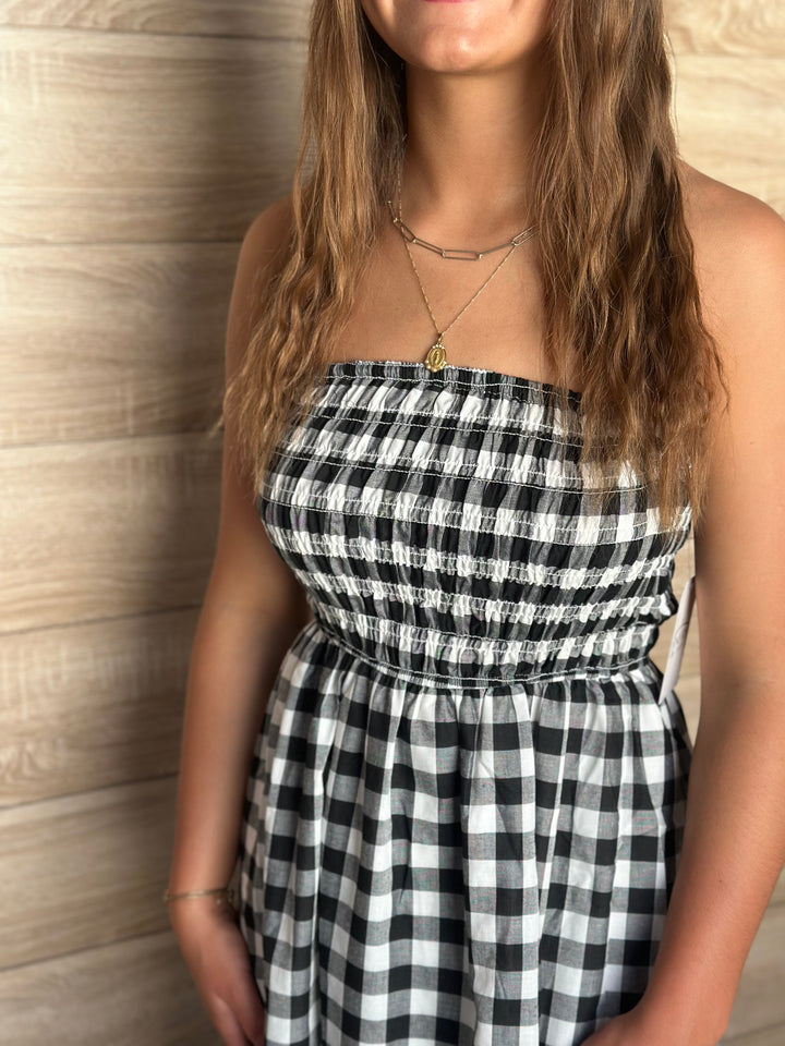 A person wearing a black and white plaid strapless dress against a wooden wall.