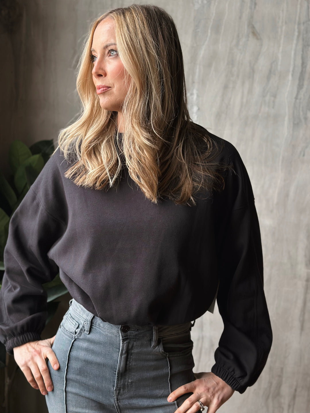 Woman wearing a black sweater and gray jeans against a neutral background
