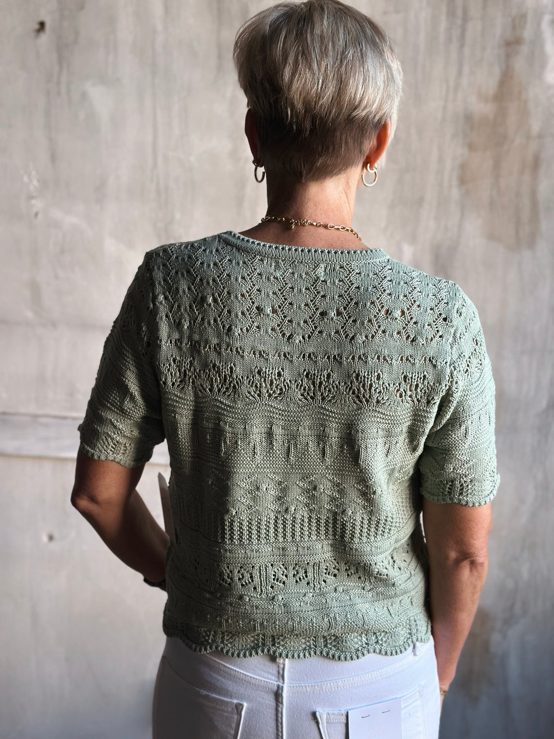 Person wearing a green knitted sweater with a textured pattern against a plain background