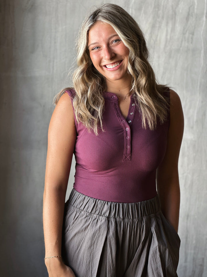Woman wearing a purple top and gray pants against a neutral background