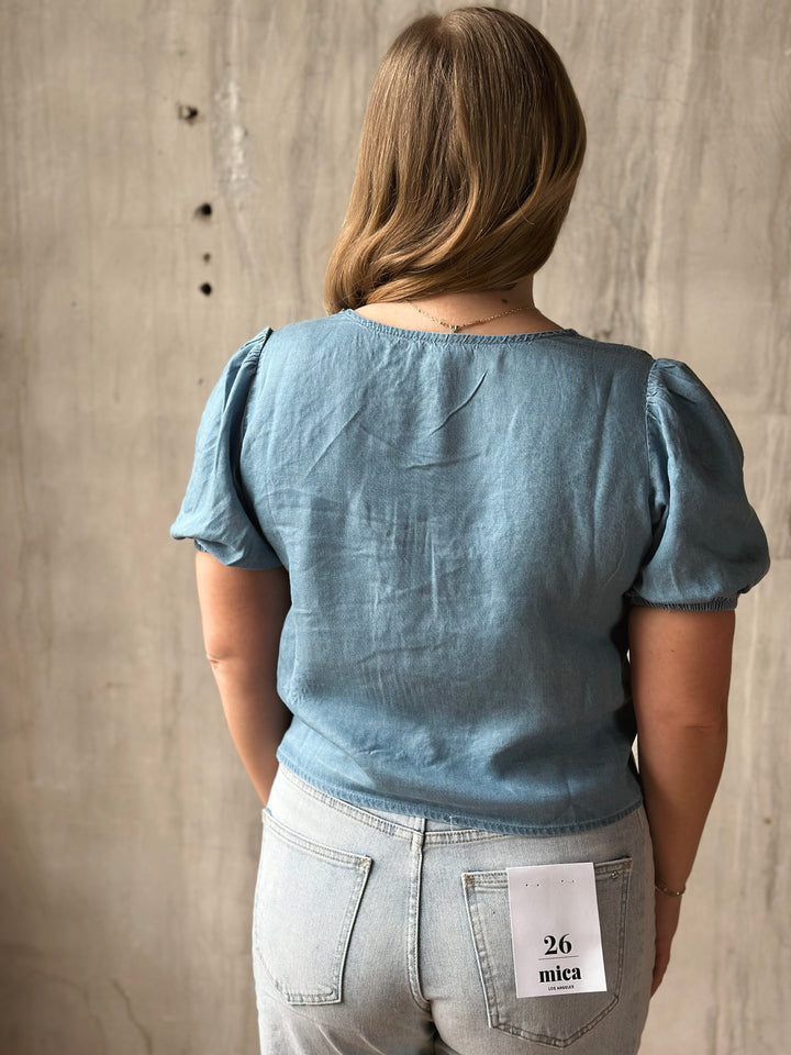 Person wearing a blue top and light blue jeans with a visible brand label against a concrete wall.
