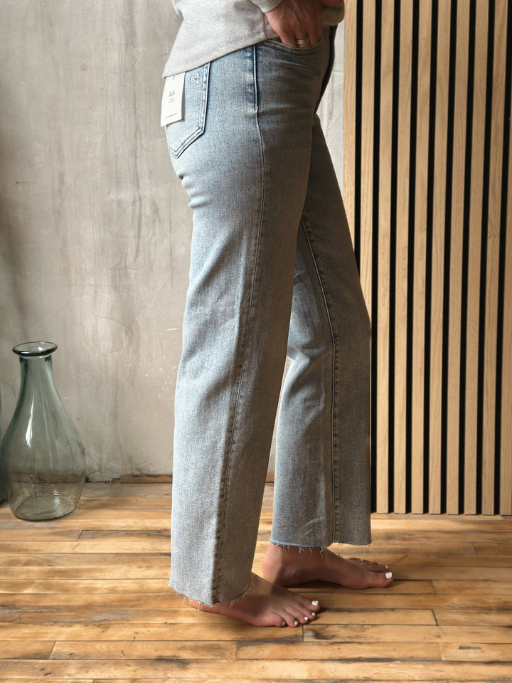 Person wearing light blue jeans standing on a wooden floor with a neutral wall background