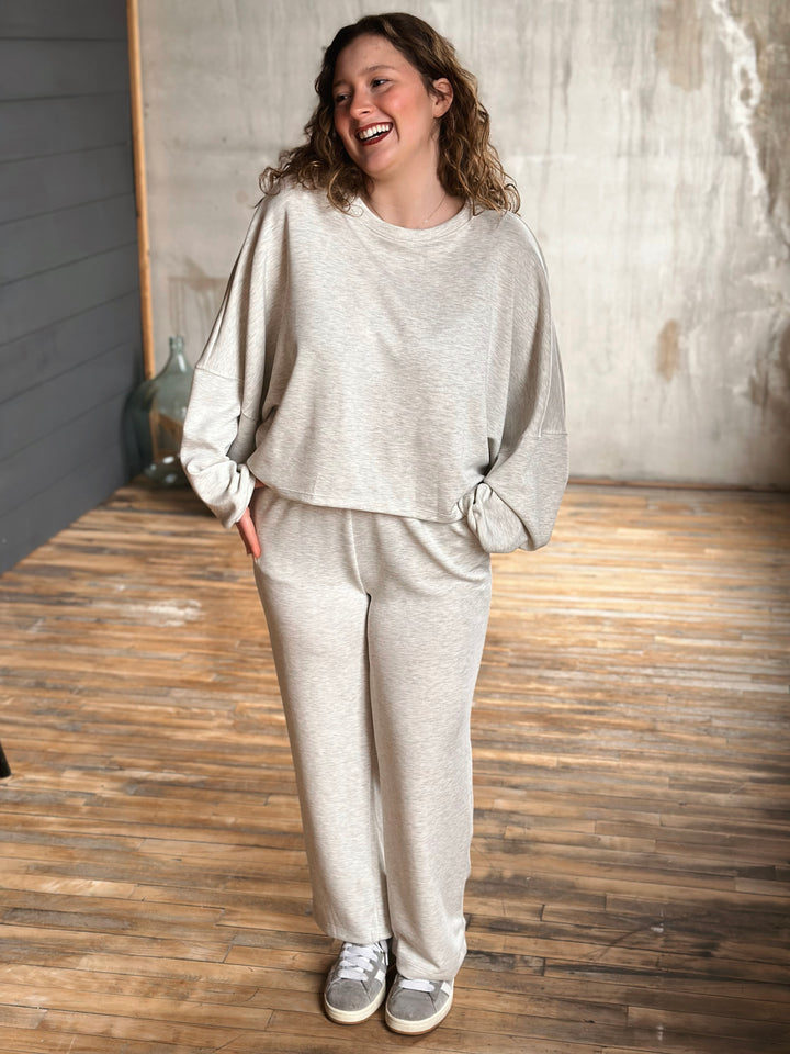 Woman wearing a light grey sweat set standing on a wooden floor.