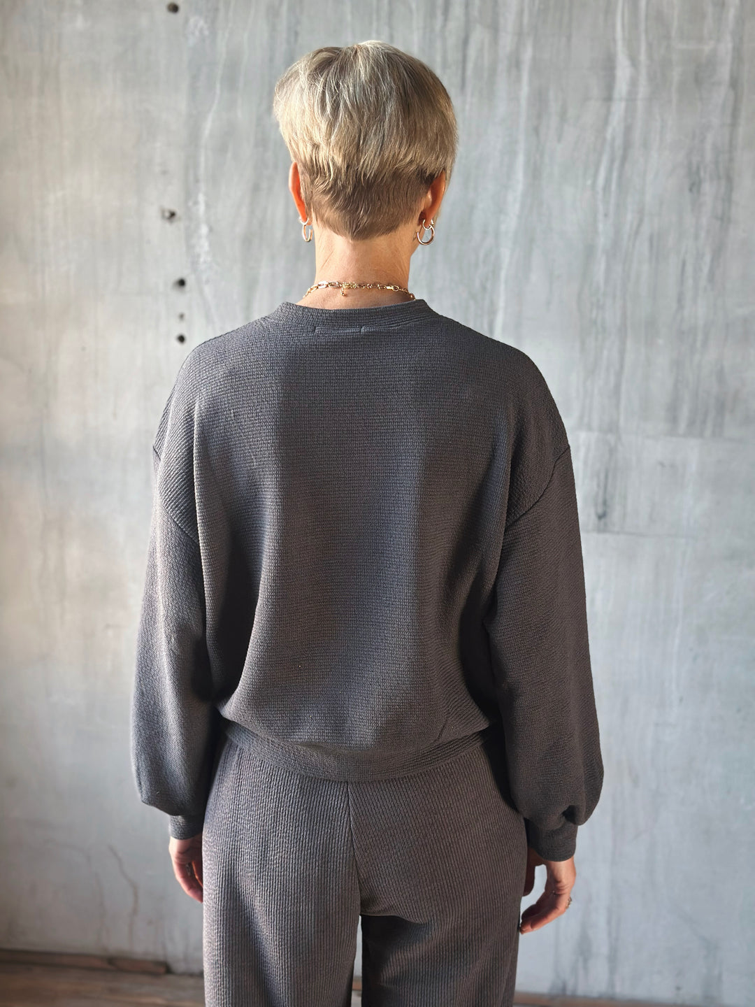 Person wearing a dark gray sweatshirt and pants against a textured wall.